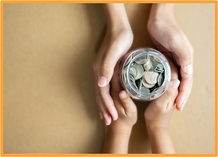 Adult and child hands holding a jar of coins, symbolizing charitable giving and financial planning in tax strategies.