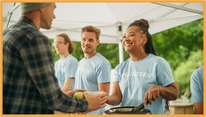Volunteers in blue shirts serving food to people outdoors, representing community service and charitable contributions.