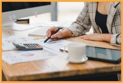 Business owner reviewing financial charts and using a calculator to prepare documents for a business loan application.