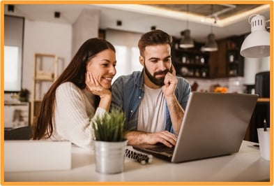 Smiling couple sitting together at a laptop, planning or reviewing details of a business trip, highlighting the importance of documenting expenses when traveling for business with your spouse.