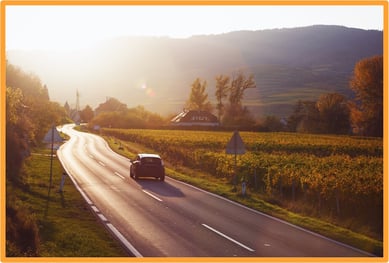 Car driving on a scenic country road, representing business travel by car with the potential for mixed business and personal travel expenses.