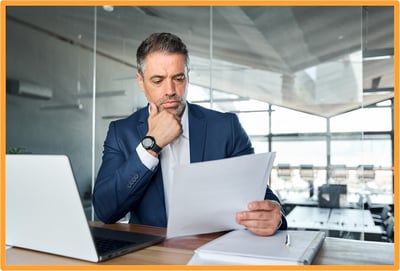 Business executive carefully reviewing financial documents and IRS guidance related to research and experimental expense deductions in a bright office setting