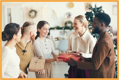 Coworkers exchanging wrapped holiday gifts in an office setting, symbolizing year-end employee appreciation and recognition.