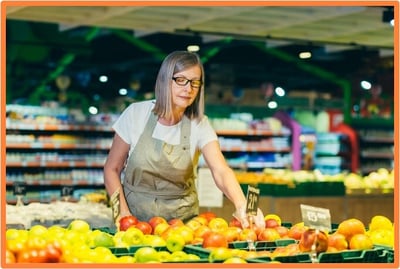 Senior woman working in a grocery store, representing the decision to continue working while receiving Social Security benefits before full retirement age