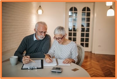 Senior couple reviewing documents and using a calculator at home, illustrating the process of planning and enrolling in Medicare.