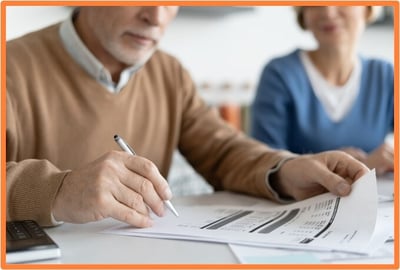Senior couple reviewing financial documents and tax forms, representing taxpayers planning investments in Qualified Opportunity Funds for tax savings under the QOZ program.