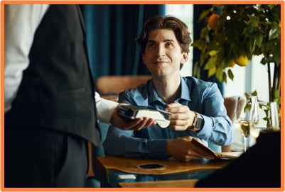 A restaurant customer paying a server with a card, illustrating qualified tips income for tax deductions under the OBBBA