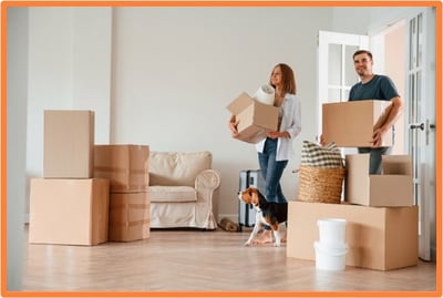 A couple moving into a new home with cardboard boxes and their dog, representing employer-paid moving expenses and relocation benefits under the OBBBA.
