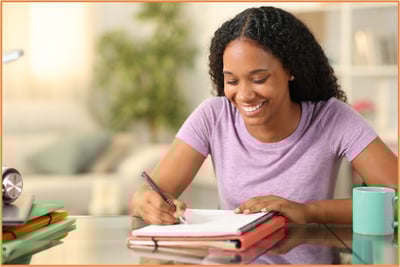 Student smiling while filling out paperwork at home, representing the FAFSA application process for college financial aid.
