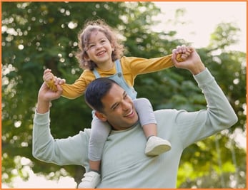 Smiling father carrying his daughter on his shoulders in a park, symbolizing positive co-parenting and family bonding after divorce or separation.