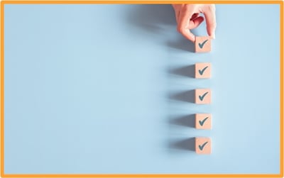 A hand placing wooden blocks with check marks in a vertical line on a blue background, representing a step-by-step tax planning checklist.
