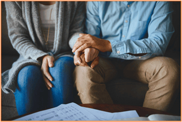 Close-up of two people sitting on a couch, holding hands in support and comfort, symbolizing emotional support during a difficult financial transition after losing a loved one.