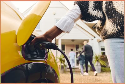 Person charging a yellow electric vehicle in front of a family home, illustrating the impact of expiring clean energy credits and incentives for electric vehicles and energy-efficient improvements in 2026.