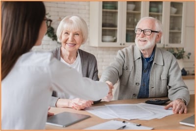 Happy retired couple meeting with a financial advisor, discussing tax planning strategies and retirement account decisions.