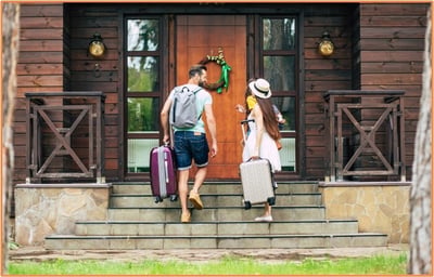 Couple carrying suitcases entering a cozy vacation rental, representing the benefits of utilizing a vacation home for rental income and charitable purposes as covered in the article.