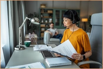 A self-employed individual wearing a headset manages paperwork and participates in a virtual meeting from a home office, representing remote work and eligible business activities for the home office deduction.