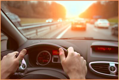 Person driving a car on a highway during sunrise or sunset, representing business travel and the importance of tracking mileage for IRS deductions.