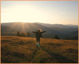 Person standing with outstretched arms in a sunlit open field, representing the freedom and beauty preserved through conservation easements.