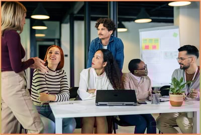 Group of five professionals engaged in a team discussion around a conference table with a laptop and documents, in a creative office environment