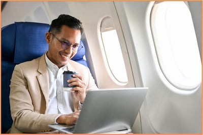 Business traveler working on a laptop and drinking coffee while seated on an airplane, illustrating modern corporate travel and the opportunities to earn frequent flyer rewards during business trips.