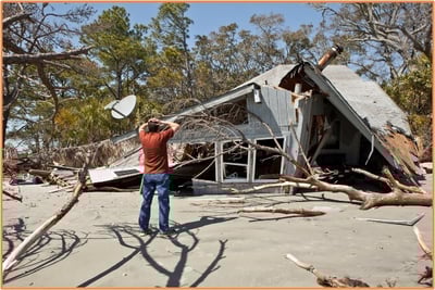 A person standing in front of a severely damaged house after a natural disaster, representing the types of federally declared disasters that may make personal theft or casualty losses tax-deductible.