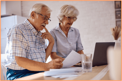 Older couple reviewing financial documents together at the kitchen table, using a laptop to plan for retirement tax breaks.
