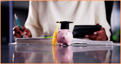 Piggy bank with graduation cap sitting on financial documents, with a person using a calculator in the background, representing new tax-advantaged savings opportunities for education and changes to 529 plans under the One Big Beautiful Bill Act.