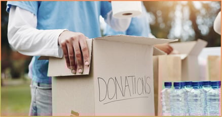 Volunteer placing items into a cardboard box labeled donations, with bottled water and supplies nearby.